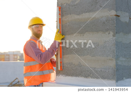 Construction worker using spirit level on building site at sunset Construction worker using spirit level on building site at sunset 141943954