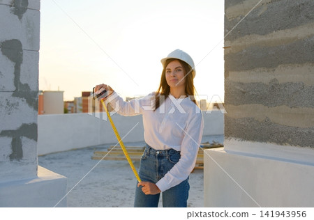 Female engineer measuring wall with tape measure at construction site during sunset Female engineer measuring wall with tape measure at construction site during sunset 141943956