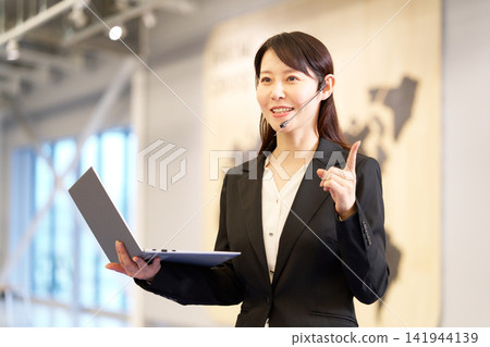 A businesswoman giving a presentation at a seminar, holding a laptop. A businesswoman giving a presentation at a seminar, holding a laptop. 141944139