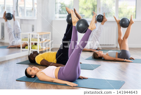 Lying and sitting on mat Asian woman coach conducts training with fitball for multinational students Lying and sitting on mat Asian woman coach conducts training with fitball for multinational students 141944643