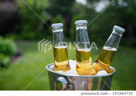 Close up of cold bottled beer in ice bucket on sunny summer backyard Close up of cold bottled beer in ice bucket on sunny summer backyard 141944735