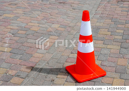 Bright Orange Traffic Safety Cone with Reflective White Stripes on a Paved Pedestrian Street Surface 141944900