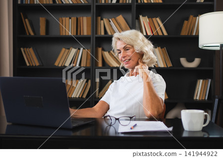 Video call. Happy middle aged senior woman sit with laptop talk on video call. Mature old senior lady having fun talking speaking online. Older generation modern tech usage Virtual meeting online chat Video call. Happy middle aged senior woman sit with laptop talk on video call. Mature old senior lady having fun talking speaking online. Older generation modern tech usage Virtual meeting online chat 141944922
