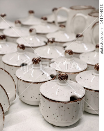 Light ceramic kitchenware including sauce dishes sugar bowls and napkin holders arranged on store shelves presenting functional everyday tableware for home serving use Light ceramic kitchenware including sauce dishes sugar bowls and napkin holders arranged on store shelves presenting functional everyday tableware for home serving use 141944958