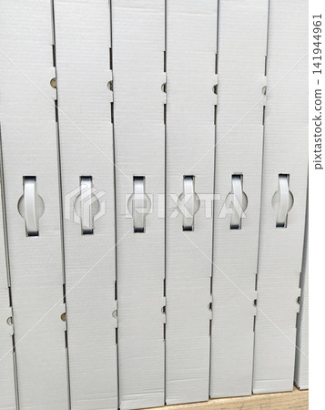 Uniform white cardboard boxes with handles stacked neatly on electronics store shelves showing organized retail packaging of consumer products in modern store environment Uniform white cardboard boxes with handles stacked neatly on electronics store shelves showing organized retail packaging of consumer products in modern store environment 141944961