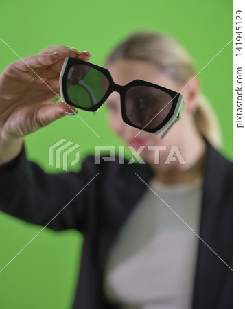 woman holding sunglasses in front of green background woman holding sunglasses in front of green background 141945129