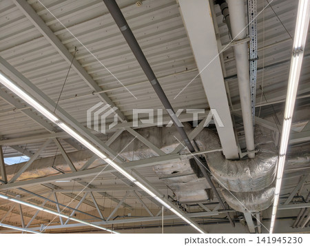 Supermarket interior featuring an advanced ceiling ventilation network, exposed pipes, and long lighting fixtures for efficient operation and comfortable shopping environment Supermarket interior featuring an advanced ceiling ventilation network, exposed pipes, and long lighting fixtures for efficient operation and comfortable shopping environment 141945230