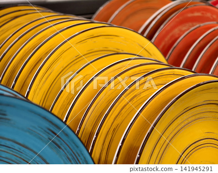 Bright red yellow and blue ceramic plates on shelves, close up of luxurious table plates for kitchen and household use Bright red yellow and blue ceramic plates on shelves, close up of luxurious table plates for kitchen and household use 141945291