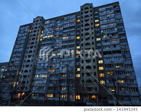 Tall residential building illuminated at night, city lights reflecting from glowing windows Tall residential building illuminated at night, city lights reflecting from glowing windows 141945345