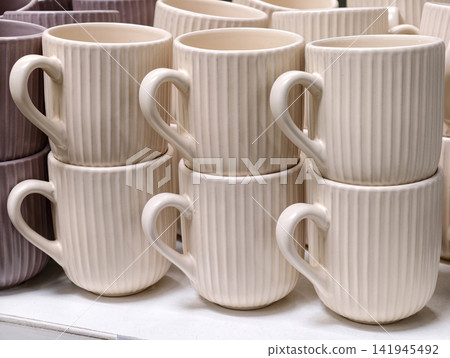 Ceramic cups arranged on retail shelves creating simple kitchenware set with functional design for everyday use and store display Ceramic cups arranged on retail shelves creating simple kitchenware set with functional design for everyday use and store display 141945492