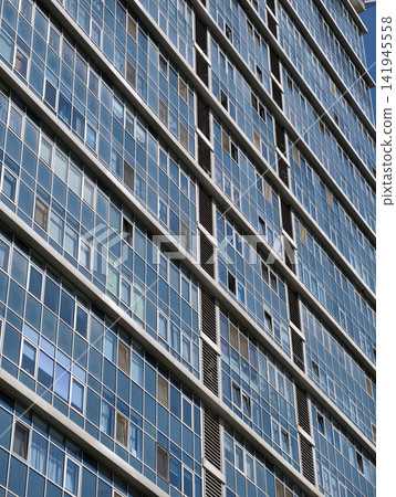 Tall blue residential skyscraper with modern engineering and numerous apartment window sections Tall blue residential skyscraper with modern engineering and numerous apartment window sections 141945558