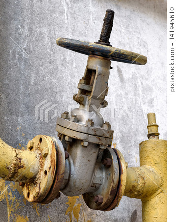 Gas shut off valve mounted on the exterior wall of a residential building with yellow pipeline and industrial utility infrastructure in urban environment Gas shut off valve mounted on the exterior wall of a residential building with yellow pipeline and industrial utility infrastructure in urban environment 141945610