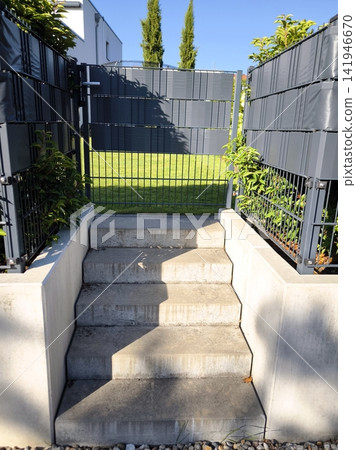 Stone steps lead to a green lawn between metal and concrete fences in the yard of a private house. Stone steps lead to a green lawn between metal and concrete fences in the yard of a private house. 141946670