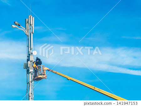 Two men, raised on a crane, will repair the power line support against the blue sky. Dangerous profession, selective focus Two men, raised on a crane, will repair the power line support against the blue sky. Dangerous profession, selective focus 141947153