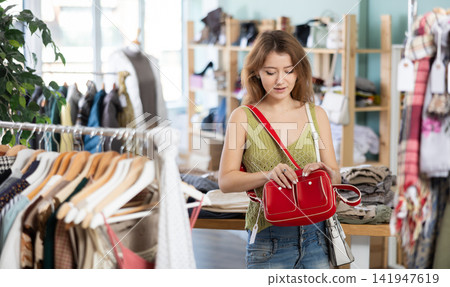 Positive young girl choosing handbag in clothing store Positive young girl choosing handbag in clothing store 141947619