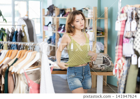 Young woman trying on top in clothing store Young woman trying on top in clothing store 141947624