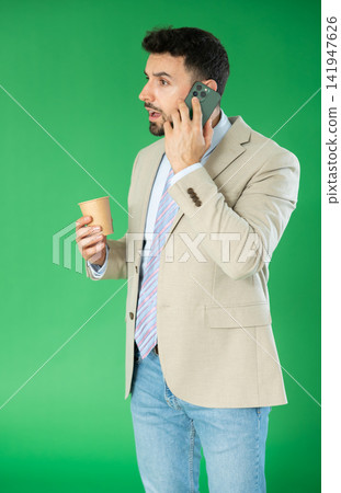 Adult man talking on phone and drinking coffee in front of green screen Adult man talking on phone and drinking coffee in front of green screen 141947626
