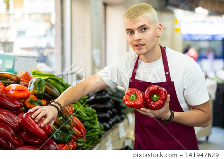 Male salesperson carefully places ripe bell peppers on a display case at grocery supermarket Male salesperson carefully places ripe bell peppers on a display case at grocery supermarket 141947629