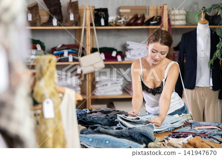 Woman shopping in clothing department, buying denim pantalones Woman shopping in clothing department, buying denim pantalones 141947670