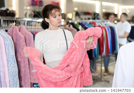 Middle-aged woman choosing convenient bathrobe in clothing store Middle-aged woman choosing convenient bathrobe in clothing store 141947703