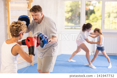 Boy and dad are boxing in gym, father helps child to work out force of blow. Boy and dad are boxing in gym, father helps child to work out force of blow. 141947732