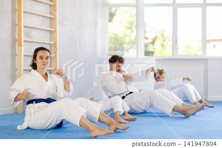 Friendly family and children train their abs and do kicks during karate lessons Friendly family and children train their abs and do kicks during karate lessons 141947804