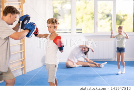 Boy and dad are boxing in gym, father helps child to work out force of blow. Boy and dad are boxing in gym, father helps child to work out force of blow. 141947813
