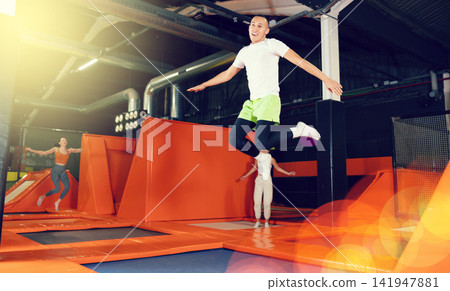 Joyful carefree young man leaping at trampoline park Joyful carefree young man leaping at trampoline park 141947881