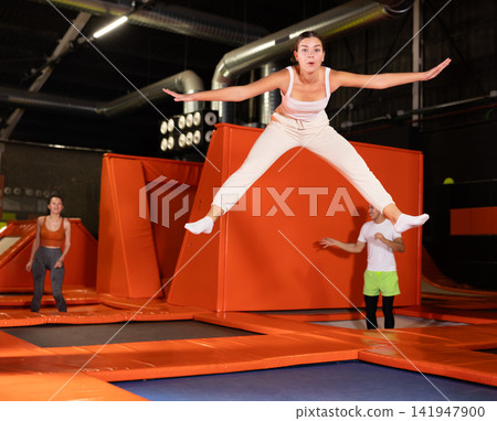 Cheerful young girl jumping in indoor trampoline arena Cheerful young girl jumping in indoor trampoline arena 141947900