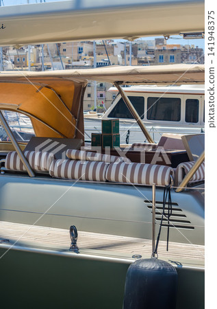 Elegant yacht deck featuring striped lounge cushions, tan canvas bimini tops, and a scenic view of a historic Mediterranean harbor town. High quality photo Elegant yacht deck featuring striped lounge cushions, tan canvas bimini tops, and a scenic view of a historic Mediterranean harbor town. High quality photo 141948375