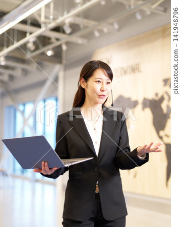 一位女商人正在研討會上演講,她手裡拿著一台筆記型電腦。 一位女商人正在研討會上演講,她手裡拿著一台筆記型電腦。 141948796