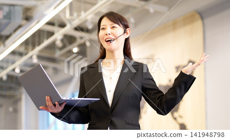 一位女商人正在研討會上演講,她手裡拿著一台筆記型電腦。 一位女商人正在研討會上演講,她手裡拿著一台筆記型電腦。 141948798