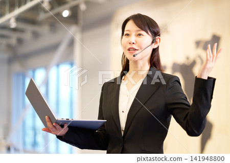 一位女商人正在研討會上演講,她手裡拿著一台筆記型電腦。 一位女商人正在研討會上演講,她手裡拿著一台筆記型電腦。 141948800