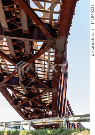 The underside structure of the red steel truss bridge, viewed from below, against the blue sky. The underside structure of the red steel truss bridge, viewed from below, against the blue sky. 141949228