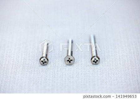 Three Phillips head screws of different lengths are lined up on a gray piece of fabric. Three Phillips head screws of different lengths are lined up on a gray piece of fabric. 141949653