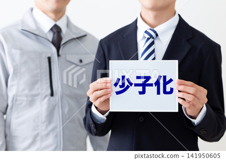 一位身穿西裝的年輕商人,手持一塊白板,上面寫著關於出生率下降的問題。 一位身穿西裝的年輕商人,手持一塊白板,上面寫著關於出生率下降的問題。 141950605