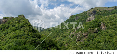 Scenic view of lush green hills and rocky formations under a cloudy sky 141951024