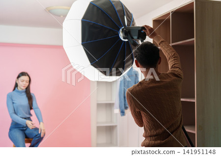Photographer setting up studio lighting for female model photoshoot Photographer setting up studio lighting for female model photoshoot 141951148