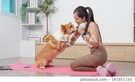 Asian woman bonding with corgi dog on yoga mat during home workout Asian woman bonding with corgi dog on yoga mat during home workout 141951158