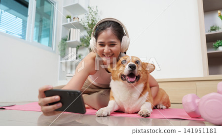 Asian woman taking selfie with corgi dog on yoga mat at home Asian woman taking selfie with corgi dog on yoga mat at home 141951181