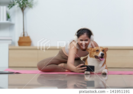 Asian woman taking selfie with Corgi dog on yoga mat at home Asian woman taking selfie with Corgi dog on yoga mat at home 141951191