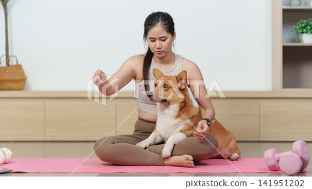 Asian woman relaxing with Corgi dog on exercise mat at home Asian woman relaxing with Corgi dog on exercise mat at home 141951202