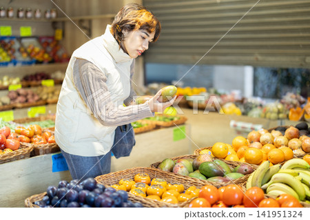 Young woman chooses mango in store Young woman chooses mango in store 141951324