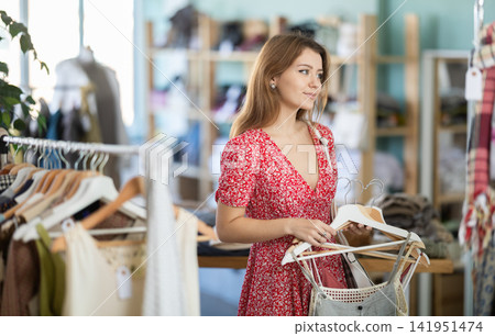 Young woman chooses dresses and tops in store Young woman chooses dresses and tops in store 141951474