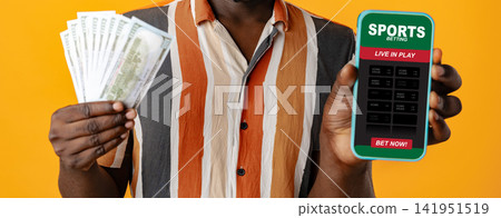 Man holding cash and mobile device showing sports betting options Man holding cash and mobile device showing sports betting options 141951519