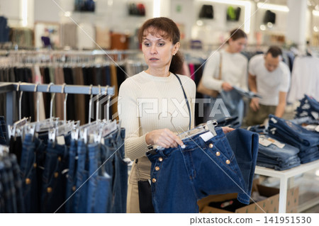 Middle-aged woman choosing blue jeans in clothing store Middle-aged woman choosing blue jeans in clothing store 141951530