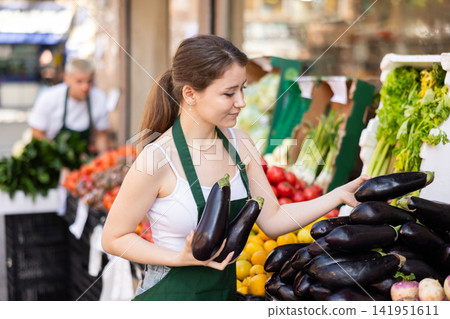 Woman seller carefully arranges eggplants Woman seller carefully arranges eggplants 141951611