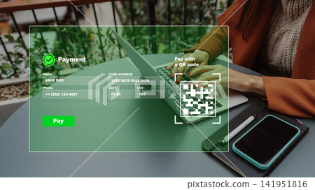 Person making an online payment using a laptop with a QR code on the screen and a phone nearby Person making an online payment using a laptop with a QR code on the screen and a phone nearby 141951816