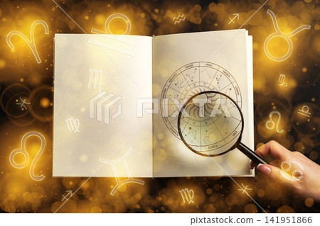 Exploring astrology zodiac signs with a magnifying glass over an open book in a warm atmosphere 141951866