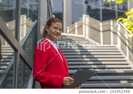 Businesswoman successful woman standing outdoor corporate building exterior. Caucasian confidence professional business woman in red suit. Businesswoman successful woman standing outdoor corporate building exterior. Caucasian confidence professional business woman in red suit. 141952348